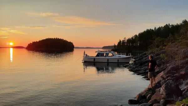 Auringonlasku järvimaisemassa, etualalla valkoinen vene rannassa.